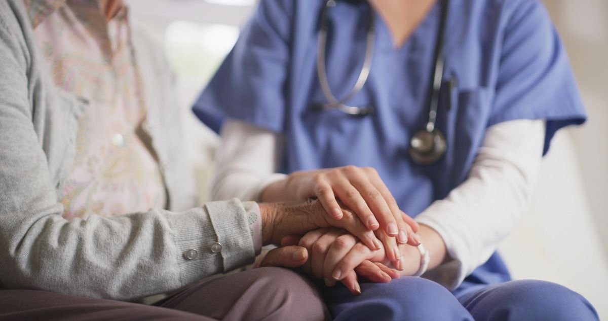 Nurse gently holding elderly patient's hands, showing care and support